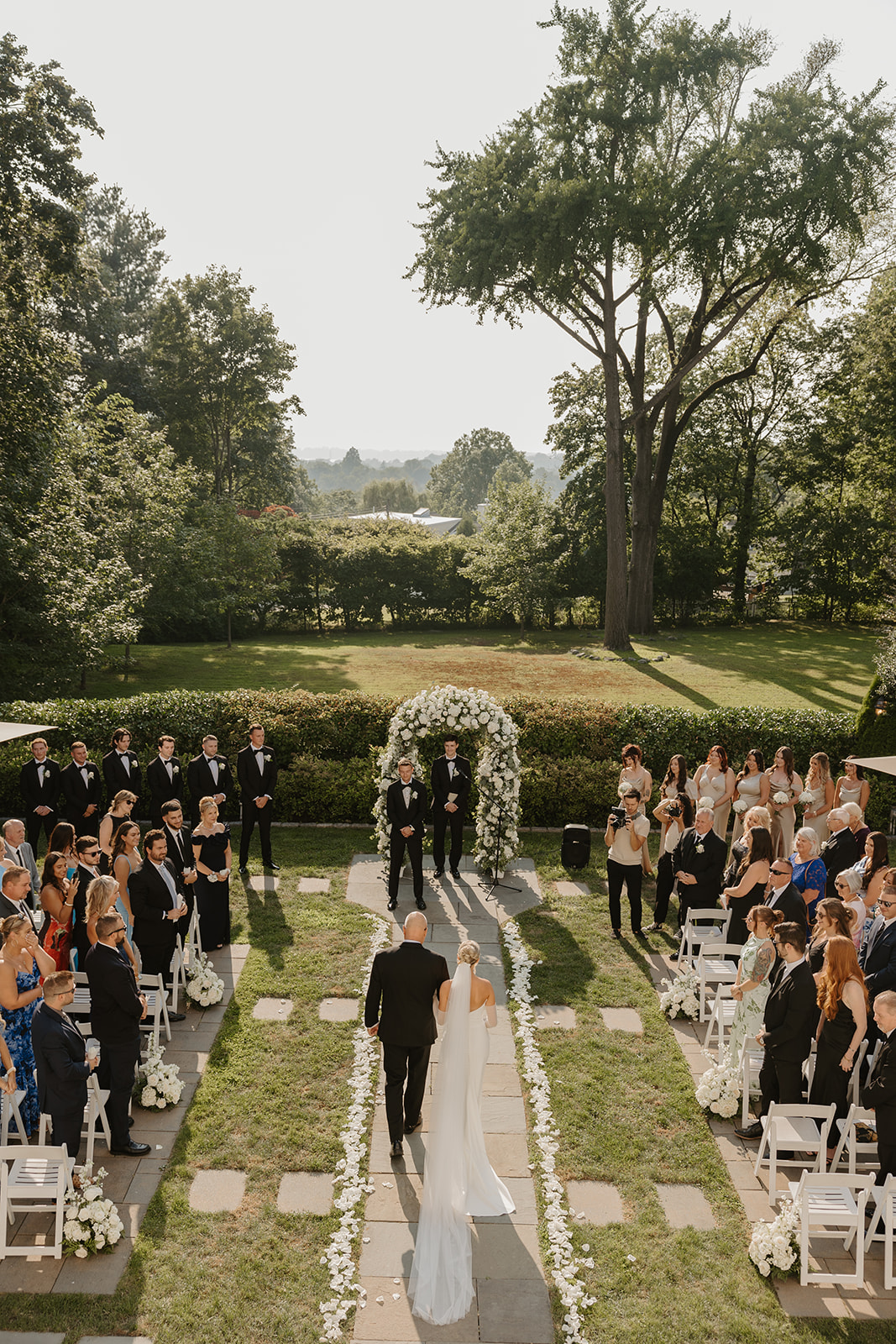 High-angle view of the bride walking down the stone aisle with her father during the outdoor ceremony.